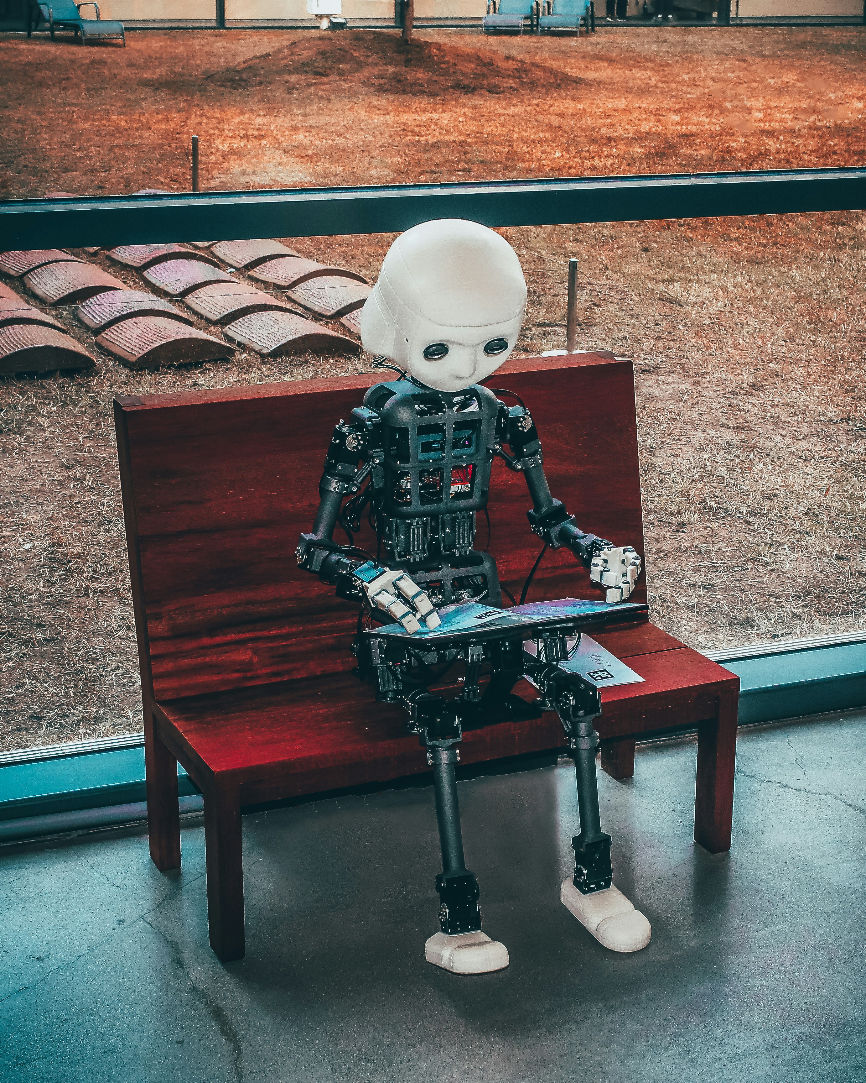 Humanoid robot sitting on bench with tablet - representing AI learning